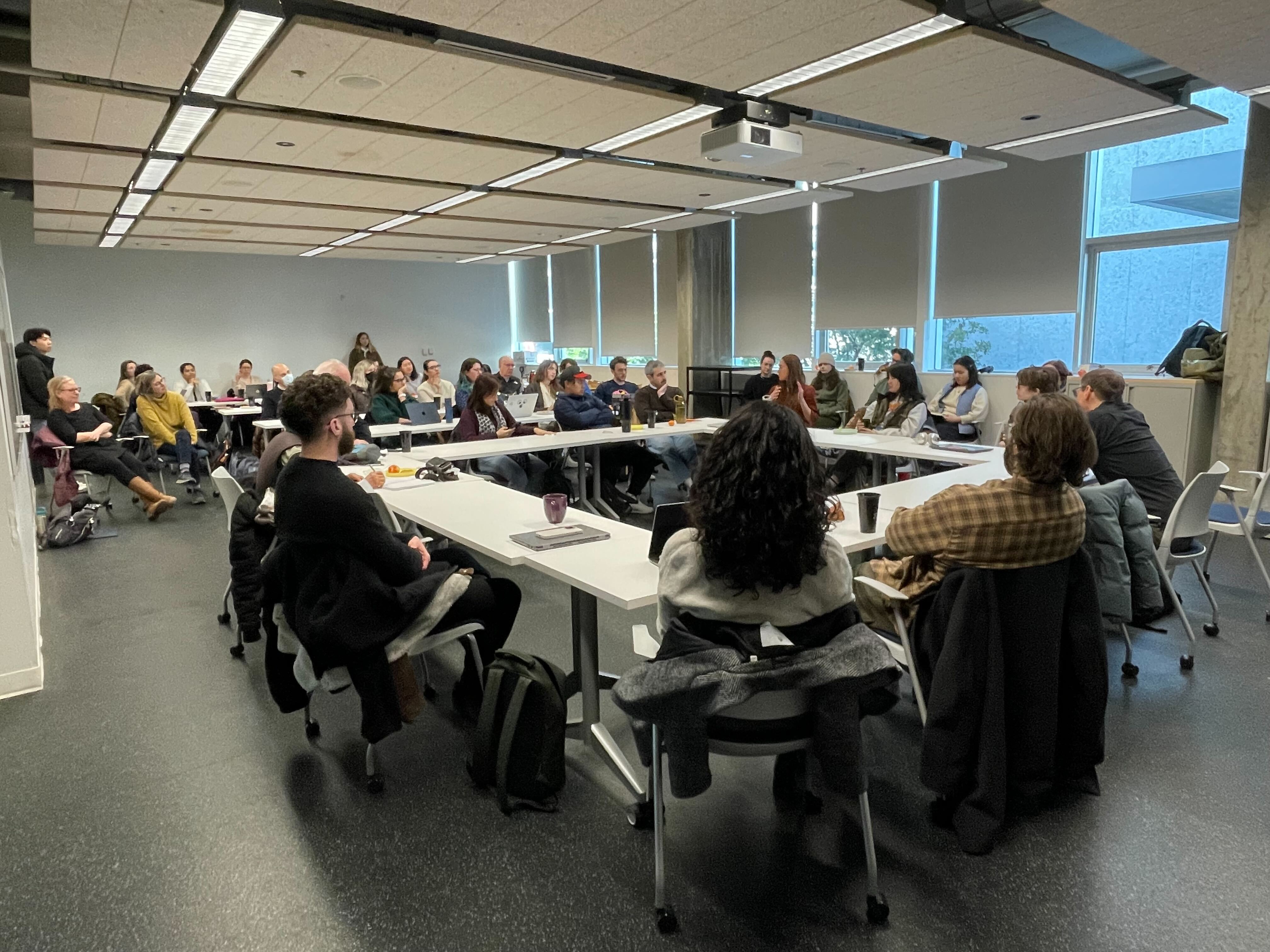 Around 50 people sit in a large room around tables