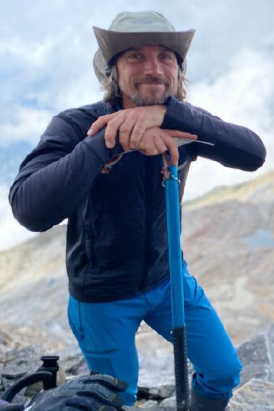 John Janmaat leans on a pickaxe, wearing a hat, in a mountain