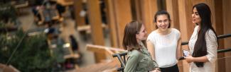 Three young people talk overlooking a wooden building interior