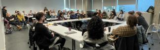 Around 50 people sit in a large room around tables