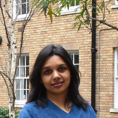 Mahfida Profile Photo_Image of smiling woman in blue sweater in front of a brick building